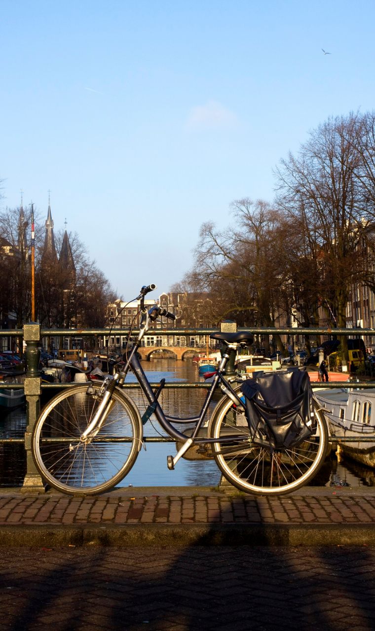Een fiets tegen de reling van een brug over een Amsterdamse gracht, in laag zonlicht